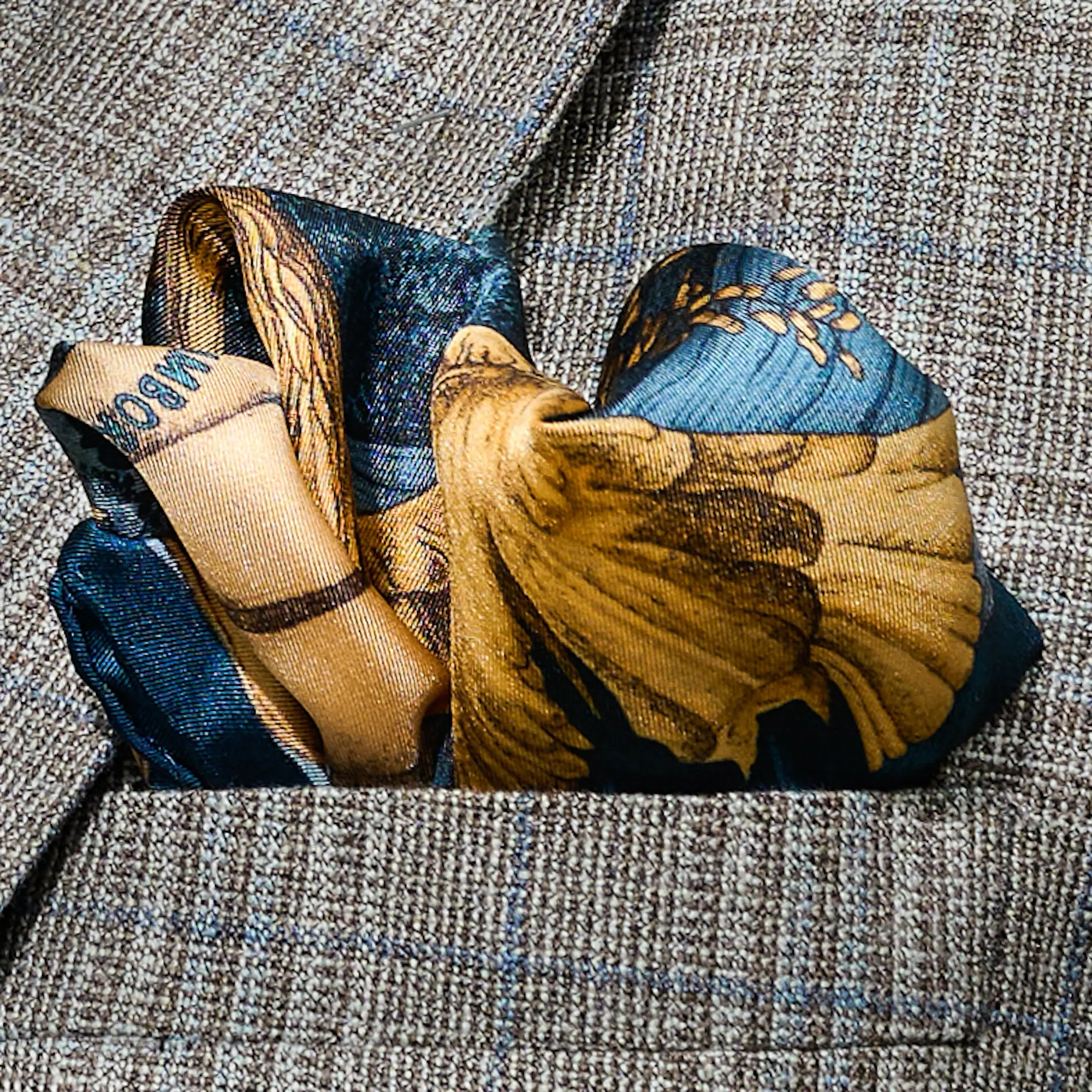 Lago di Como Navy Blue Silk Pocket Square folded in a jacket pocket — luxury hand-rolled edge, deep navy and gold tones, handmade in Italy.